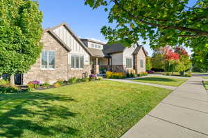 Craftsman inspired home with board and batten siding, a front yard, stone siding, covered porch, and roof with shingles