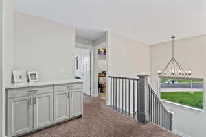 Hallway featuring dark colored carpet, a chandelier, and an upstairs landing