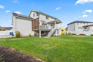 Back of property with a fenced backyard, stairs, a wooden deck, roof mounted solar panels, and a residential view