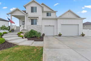 View of front of property with board and batten siding, concrete driveway, and stone siding