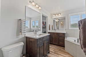 Full bathroom with plenty of natural light, a garden tub, two vanities, and light wood-style floors