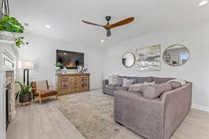 Living room featuring wooden walls, recessed lighting, ceiling fan, light wood-style floors, and a fireplace