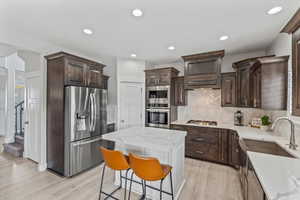 Kitchen featuring dark brown cabinets, appliances with stainless steel finishes, light stone countertops, light wood-style flooring, and recessed lighting
