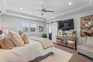 Bedroom with a barn door, a tray ceiling, carpet floors, a ceiling fan, and recessed lighting