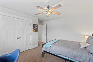 Carpeted bedroom with ceiling fan and a closet