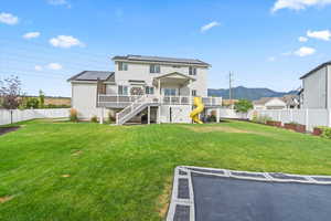 Rear view of house featuring solar panels, a fenced backyard, stairway, a playground, and a deck with mountain view