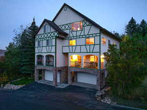 Tudor house with stone siding, a balcony, an attached garage, driveway, and stucco siding