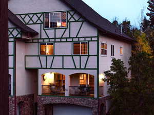 Back of property with stucco siding, a shingled roof, stone siding, and a balcony