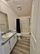 Bathroom with a textured ceiling, vanity, shower / bath combination with curtain, and light wood finished floors