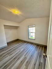 Unfurnished bedroom with light wood-type flooring, a textured ceiling, lofted ceiling, and a closet