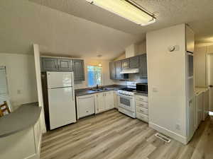 Kitchen featuring a textured ceiling, white appliances, vaulted ceiling, light wood-style floors, and gray cabinetry