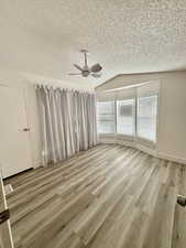 Street facing bedroom with lofted ceiling, light wood-type flooring, ceiling fan, and a textured ceiling
