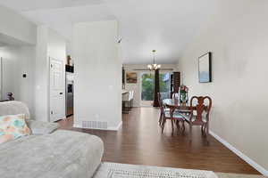 Living room looking into dining/kitchen area with dark wood finished floors and a chandelier