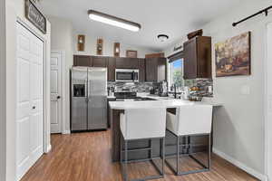 Kitchen featuring dark brown cabinets, stainless steel appliances, lofted ceiling, light countertops, and a breakfast bar area