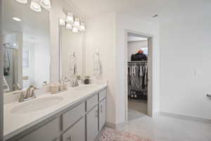 Full bathroom with light tile patterned floors, double vanity, a walk in closet, and a shower