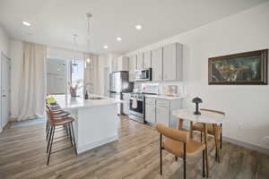 Kitchen featuring stainless steel appliances, a kitchen island with sink, hanging light fixtures, a kitchen breakfast bar, and decorative backsplash