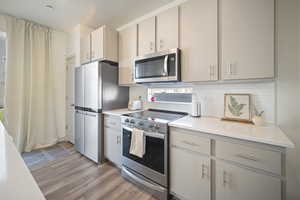 Kitchen featuring stainless steel appliances, decorative backsplash, light wood finished floors, and plenty of natural light