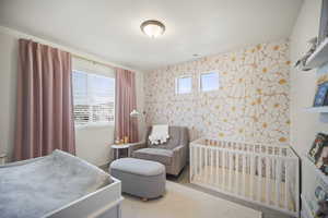 Bedroom with wallpapered walls, multiple windows, an accent wall, and a nursery area