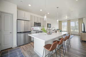 Kitchen with appliances with stainless steel finishes, hanging light fixtures, light wood-type flooring, an island with sink, and a breakfast bar