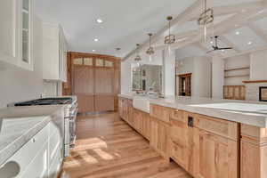 Kitchen featuring light brown cabinetry, stainless steel stove, decorative light fixtures, light wood-type flooring, and white cabinetry