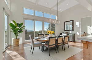 Virtually Staged - Dining space with light wood-type flooring, beam ceiling, a towering ceiling, and a chandelier
