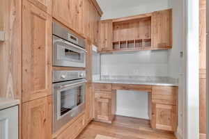 Kitchen with open shelves, light wood-style flooring, light brown cabinets, light countertops, and double oven