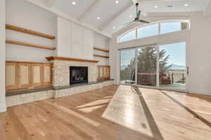 Unfurnished living room featuring light wood-type flooring, beam ceiling, a fireplace, high vaulted ceiling, and ceiling fan