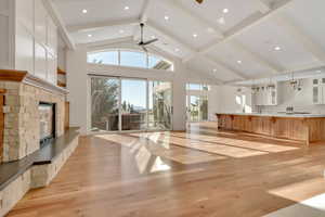 Unfurnished living room with light wood finished floors, a fireplace, plenty of natural light, high vaulted ceiling, and a ceiling fan
