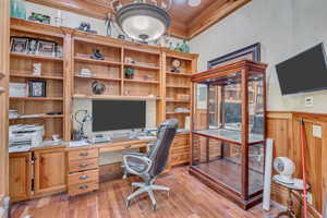 Office area with ornamental molding, light wood finished floors, and built in desk