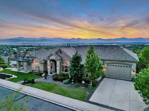 French country inspired facade with stone siding, a garage, concrete driveway, a mountain view, and a lawn