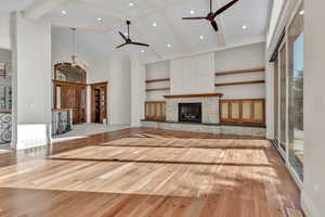 Unfurnished living room featuring a stone fireplace, wood finished floors, high vaulted ceiling, a ceiling fan, and beam ceiling