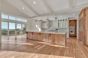 Kitchen with beam ceiling, a kitchen breakfast bar, light wood finished floors, glass insert cabinets, and a spacious island