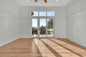 Unfurnished living room with a decorative wall, crown molding, a ceiling fan, light wood-style flooring, and wainscoting