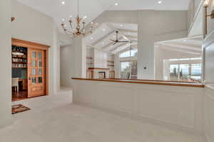 Unfurnished dining area with a chandelier, a ceiling fan, high vaulted ceiling, a fireplace, and an office area