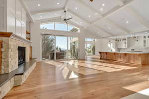 Unfurnished living room with light wood-style flooring, a fireplace, ceiling fan, beamed ceiling, and high vaulted ceiling
