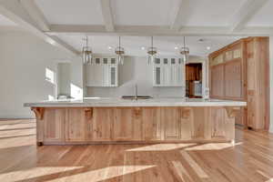 Kitchen featuring a breakfast bar area, light brown cabinetry, beam ceiling, glass insert cabinets, and light wood-style flooring