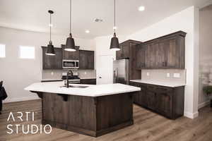 Kitchen featuring dark brown cabinets, decorative backsplash, appliances with stainless steel finishes, light stone counters, and pendant lighting