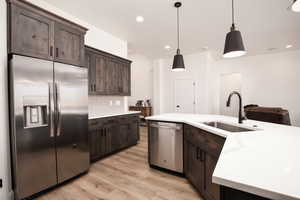 Kitchen with stainless steel appliances, backsplash, dark brown cabinetry, light stone countertops, and decorative light fixtures
