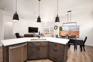Kitchen with dark brown cabinets, stainless steel dishwasher, light wood-style floors, pendant lighting, and a kitchen island with sink