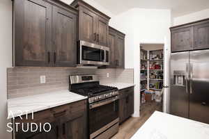 Kitchen featuring appliances with stainless steel finishes, dark brown cabinets, light wood-style floors, and light stone counters