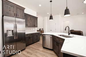 Kitchen featuring tasteful backsplash, appliances with stainless steel finishes, dark brown cabinetry, light stone countertops, and hanging light fixtures