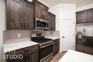 Kitchen featuring stainless steel appliances, light stone countertops, dark brown cabinetry, and light wood-type flooring