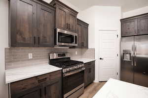 Kitchen with stainless steel appliances, light stone counters, light wood-type flooring, dark brown cabinetry, and tasteful backsplash