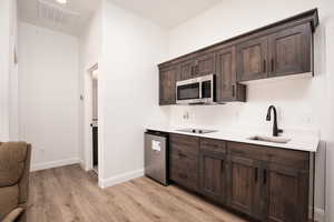 Kitchen with dark brown cabinetry, stainless steel appliances, light wood-style flooring, and light stone counters