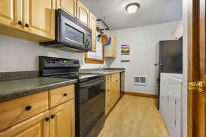 Kitchen with black appliances, light wood-type flooring, a textured ceiling, and dark countertops