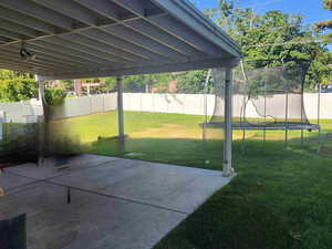 Fenced backyard featuring a trampoline and a patio area