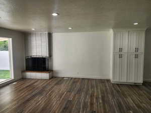 Unfurnished living room featuring a textured ceiling, a fireplace, dark wood-style floors, and recessed lighting