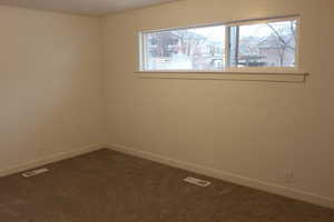 Spare room featuring dark colored carpet and baseboards