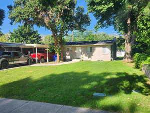 Single story home featuring a front lawn, brick siding, a chimney, and a carport