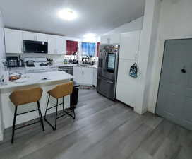 Kitchen featuring a textured ceiling, stainless steel appliances, white cabinets, a breakfast bar area, and vaulted ceiling